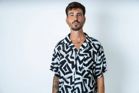 Photo for Shot of pleasant looking man with tattoo wearing summer shirt standing over isolated white background with pouts lips, looks at camera, Human facial expressions - Royalty Free Image