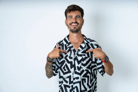 Foto de Hombre con tatuaje vistiendo camisa de verano de pie sobre aislados puntos de fondo blanco en su cuerpo, estar de buen humor después de ir de compras y hacer compras exitosas - Imagen libre de derechos