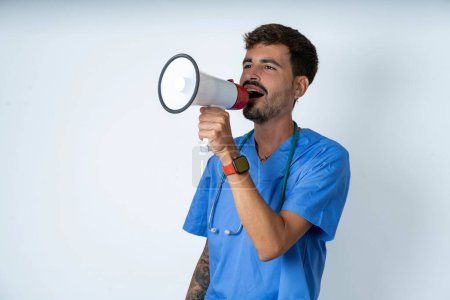 Téléchargez les photos : Belle infirmière homme portant uniforme de chirurgien sur fond blanc à travers mégaphone avec l'espace de copie disponible - en image libre de droit