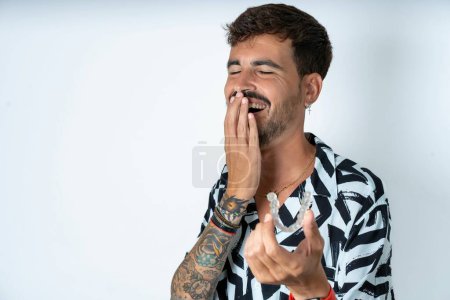 Téléchargez les photos : Heureux jeune homme caucasien portant chemise imprimée tenant et montrant à la caméra un aligneur invisible tout en riant. Concept de soins dentaires et de confiance. - en image libre de droit