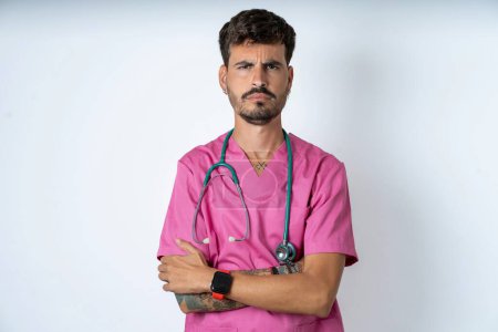 Photo for Gloomy dissatisfied young caucasian doctor man wearing pink medical uniform looks with miserable expression at camera from under forehead, makes unhappy grimace - Royalty Free Image