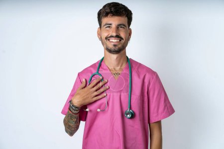 Foto de Guapo enfermero vistiendo uniforme de cirujano sobre fondo blanco sonríe con dientes no puedo creer ojos expresa buenas emociones y sorpresa - Imagen libre de derechos