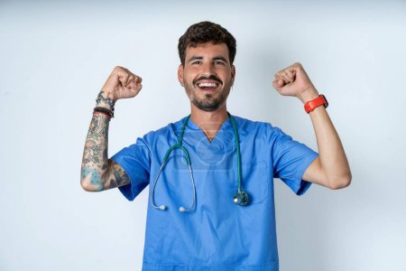 Foto de Guapo enfermera hombre vistiendo cirujano uniforme sobre blanco fondo mostrando músculo - Imagen libre de derechos