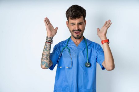 Photo for Handsome nurse man wearing surgeon uniform over white background goes crazy as head goes around feels stressed because of horrible situation - Royalty Free Image