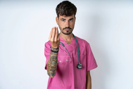 Foto de Guapo enfermero vistiendo uniforme de cirujano sobre fondo blanco haciendo gesto italiano con la mano y los dedos expresión confiada - Imagen libre de derechos
