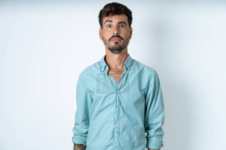 Photo for Stunned handsome young man wearing turquoise shirt over white background stares reacts on shocking news. Astonished man holds breath - Royalty Free Image