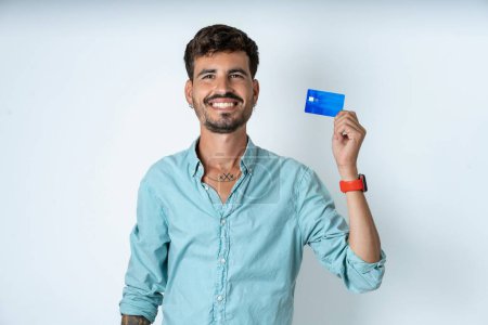 Photo for Photo of happy cheerful smiling positive handsome young man wearing turquoise shirt over white background recommend credit card - Royalty Free Image