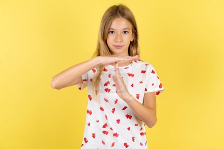 Photo for Caucasian kid girl wearing polka dot shirt over yellow background being upset showing a timeout gesture, needs stop, asks time for rest after hard work, - Royalty Free Image