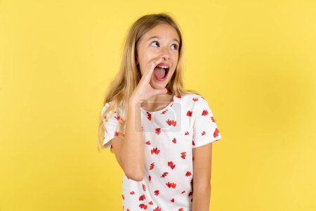 Photo for Caucasian kid girl wearing polka dot shirt over yellow background hear incredible private news impressed scream share - Royalty Free Image