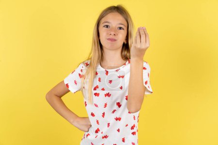 Téléchargez les photos : Enfant caucasien fille portant chemise à pois sur fond jaune geste de colère geste italien typique avec la main, regardant à la caméra - en image libre de droit