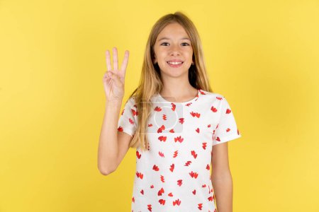 Photo for Caucasian kid girl wearing polka dot shirt over yellow background showing and pointing up with fingers number three while smiling confident and happy. - Royalty Free Image