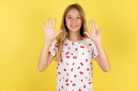 Foto de Niña caucásica con camisa de lunares sobre fondo amarillo mostrando y apuntando hacia arriba con los dedos número nueve mientras sonríe confiado y feliz. - Imagen libre de derechos