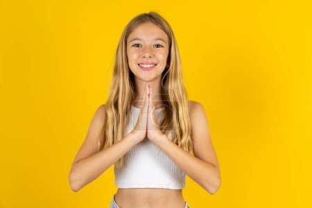 Photo for Blonde girl wearing white T-shirt over yellow background praying with hands together asking for forgiveness smiling confident. - Royalty Free Image