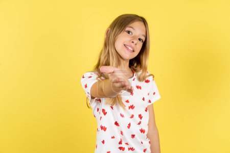 Foto de Niña caucásica con camisa de lunares sobre fondo amarillo sonriente amistoso ofreciendo apretón de manos como saludo y bienvenida. Negocios exitosos. - Imagen libre de derechos