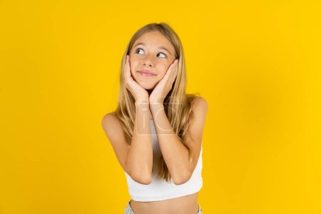 Inspired blonde girl wearing white T-shirt over yellow background looking at copyspace having thoughts about future events