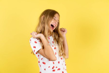 Foto de Extático caucásico niño chica usando polka punto camisa sobre amarillo fondo grito fuerte sí puño arriba levantar ganar lotería - Imagen libre de derechos