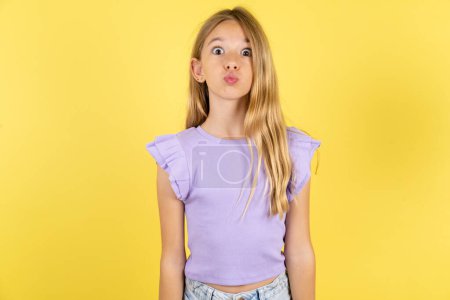 Photo for Shot of pleasant looking blonde girl wearing violet T-shirt over yellow background pouts lips, looks at camera, Human facial expressions - Royalty Free Image