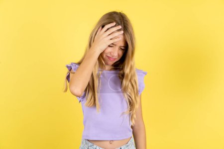 Téléchargez les photos : Une fille blonde très contrariée et solitaire portant un T-shirt violet sur fond jaune qui pleure - en image libre de droit