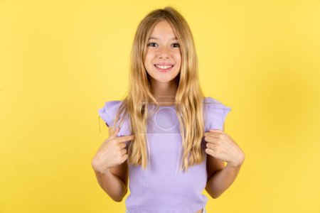Foto de Chica rubia vistiendo camiseta violeta sobre puntos amarillos de fondo en su cuerpo, estar de buen humor después de ir de compras y hacer compras exitosas - Imagen libre de derechos