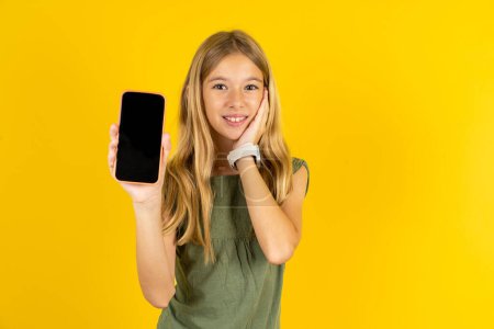 Photo for Blond little girl wearing khaki blouse over yellow background  hold hand modern technology use touch face palm astonished impressed scream wow omg unbelievable unexpected - Royalty Free Image