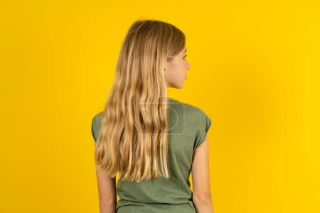 Photo for The back side view of a blond little girl wearing khaki blouse over yellow background. Studio Shoot. - Royalty Free Image