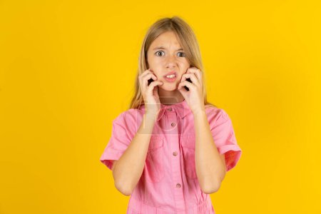 Photo for Speechless girl wearing pink jacket over yellow background  keeps hands near opened mouth reacts to shocking news stares wondered at camera - Royalty Free Image