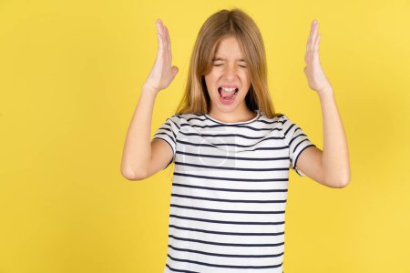 Photo for Beautiful caucasian teen girl wearing striped T-shirt over yellow background goes crazy as head goes around feels stressed because of horrible situation - Royalty Free Image