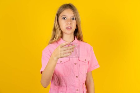 Téléchargez les photos : Fille choquée portant une veste rose sur fond jaune points à vous avec une expression stupéfaite - en image libre de droit
