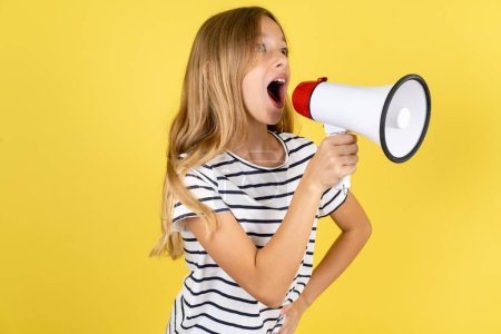 Photo for Funny beautiful caucasian teen girl wearing striped T-shirt over yellow background People sincere emotions lifestyle concept. Mock up copy space. Screaming in megaphone. - Royalty Free Image