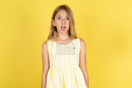 Téléchargez les photos : Fille choquée portant robe jaune sur fond jaune fixe les yeux buggés garde la bouche ouverte a une expression surprise. Concept d'Omg - en image libre de droit