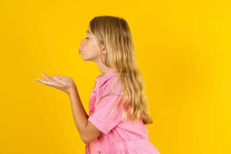 Téléchargez les photos : Profil vue de côté, portrait d'une jolie fille portant une veste rose sur fond jaune envoyant un baiser d'air - en image libre de droit