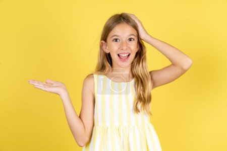 Foto de Sorprendido sorprendido chica sorprendida con vestido amarillo sobre fondo amarillo sostener la mano ofreciendo proposición - Imagen libre de derechos