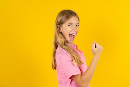 Photo for Profile side view portrait girl wearing pink jacket over yellow background celebrates victory - Royalty Free Image