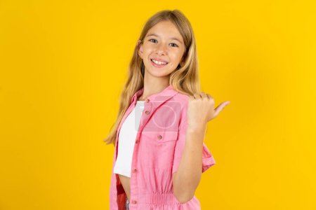 Photo for Impressed girl wearing pink jacket over yellow background point back empty space - Royalty Free Image