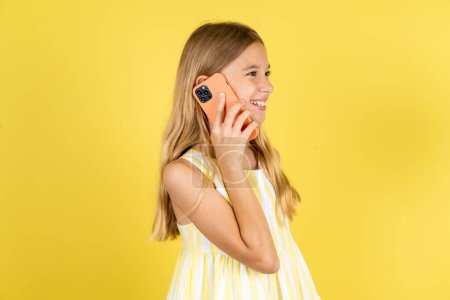 Téléchargez les photos : Joyeux joyeux charmant fille portant robe jaune sur fond jaune parler parler téléphone sourire de bonne humeur - en image libre de droit
