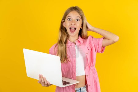 Téléchargez les photos : Photo de fille étonnée portant une veste rose sur fond jaune tenant la tête de bras gadget moderne - en image libre de droit