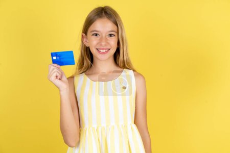 Photo for Photo of happy cheerful smiling positive girl wearing yellow dress over yellow background recommend credit card - Royalty Free Image