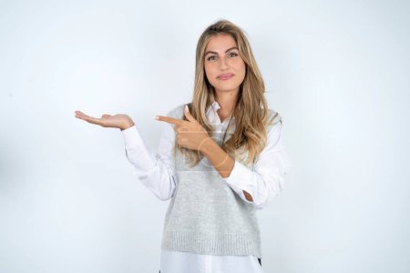 Foto de Hermosa mujer de negocios rubia hispana sobre fondo blanco señalando y sosteniendo la mano mostrando anuncios - Imagen libre de derechos