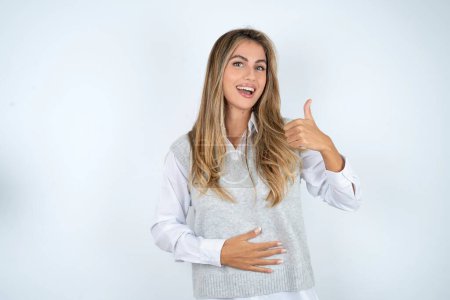 Téléchargez les photos : Belle hispanique blonde femme d'affaires sur fond blanc heureux sourire positif mains sur le ventre montrer pouce vers le haut bien sain - en image libre de droit