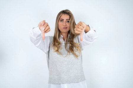 Photo for Beautiful hispanic blonde businesswoman over white background  being upset showing thumb down with two hands. Dislike concept. - Royalty Free Image
