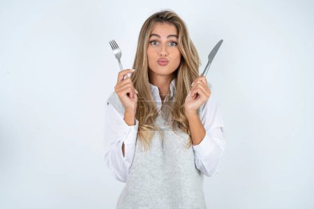 Photo for Hungry beautiful hispanic blonde businesswoman over white background holding in hand fork knife want tasty yummy pizza pie - Royalty Free Image