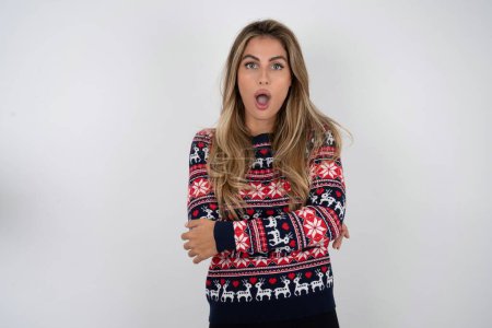 Photo for Shocked embarrassed beautiful blonde woman wearing knitted christmas sweater keeps mouth widely opened. Hears unbelievable novelty stares in stupor - Royalty Free Image