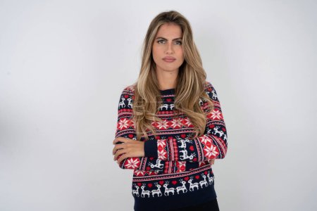 Photo for Gloomy dissatisfied beautiful blonde woman wearing knitted christmas sweater looks with miserable expression at camera from under forehead, makes unhappy grimace - Royalty Free Image