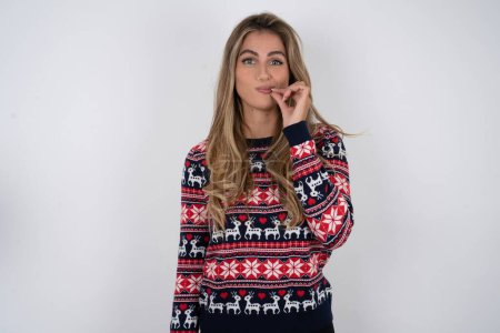Photo for Beautiful blonde woman wearing knitted christmas sweater making quiet gesture - Royalty Free Image