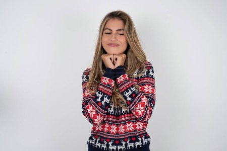 Foto de Alegre hermosa mujer rubia con suéter de Navidad de punto tiene tímida expresión satisfecha, sonríe ampliamente, muestra dientes blancos, emociones de la gente - Imagen libre de derechos