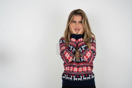Téléchargez les photos : Portrait de femme blonde triste portant un pull de Noël tricoté avec les mains sur le visage - en image libre de droit