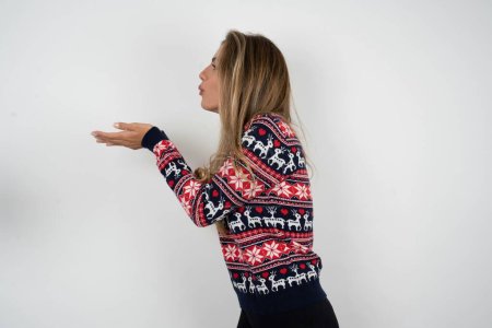 Téléchargez les photos : Profil vue de côté, portrait d'une jolie belle femme blonde portant un pull de Noël tricoté envoyant un baiser d'air - en image libre de droit