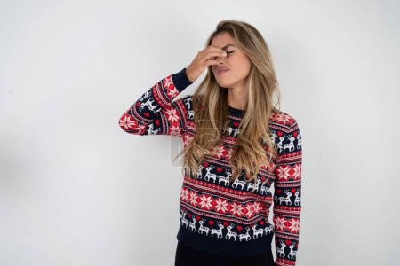 Photo for Sad beautiful blonde woman wearing knitted christmas sweater suffering from headache holding hand on her face - Royalty Free Image