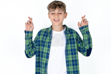 Photo for Handsome teen boy wearing plaid shirt over white background has big hope, crosses fingers, believes in good fortune, smiles broadly. People and wish concept - Royalty Free Image