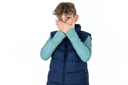 Téléchargez les photos : Beau garçon adolescent caucasien en gilet bleu choqué couvrant la bouche avec les mains pour erreur. Concept secret. - en image libre de droit